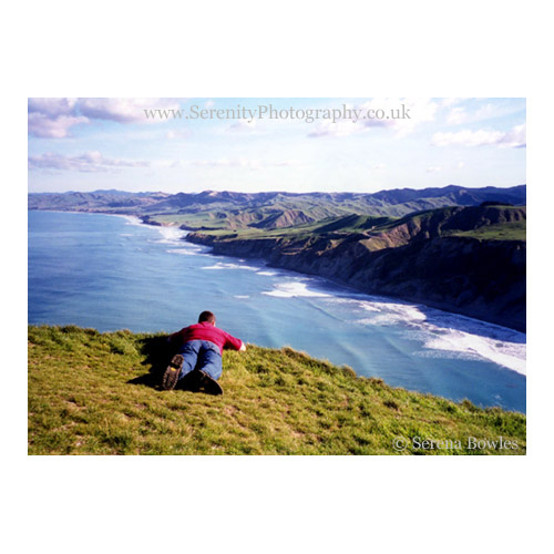 A boy lies on the edge of the cliff, watching the waves below at Castlepoint on the North Island of New Zealand